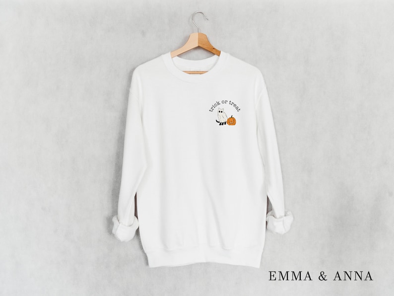 May include: White sweatshirt with long sleeves and a crew neck. The sweatshirt has a small embroidered design on the front that says "trick or treat" with a ghost and a pumpkin.