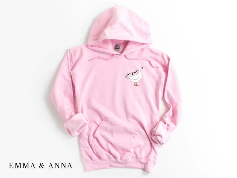 K&ouml;nnte beinhalten: Ein rosa Kapuzenpullover mit einem wei&szlig;en G&auml;nse-Motiv und dem Text "silly goose" auf der Vorderseite.