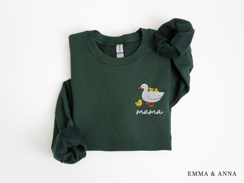 May include: A dark green sweatshirt with a white embroidered goose and ducklings. The text "mama" is embroidered below the goose.