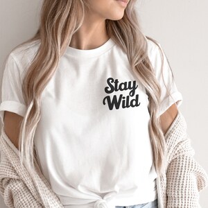 May include: White t-shirt with black text that reads "Stay Wild" in a retro font.