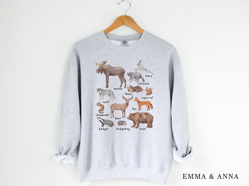 May include: A gray sweatshirt with a graphic print of various woodland animals, including a moose, wolf, deer, fox, bear, raccoon, squirrel, chipmunk, badger, hedgehog, and hare. The animals are illustrated in a realistic style with brown, black, white, and gray colors.