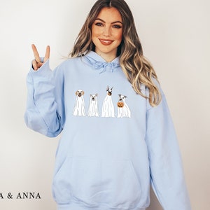 May include: A light blue hoodie featuring a graphic of four dogs dressed as ghosts for Halloween. The dogs are a Labrador Retriever, a Doberman Pinscher, a Jack Russell Terrier, and a Dachshund.