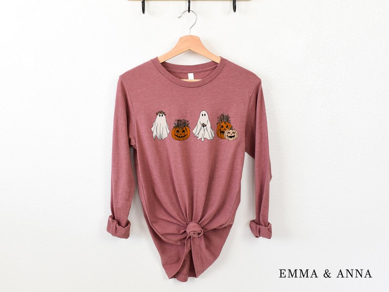 May include: A long-sleeved mauve t-shirt with a graphic of ghosts and pumpkins wearing floral crowns. The shirt is tied in a knot at the bottom.