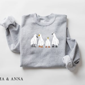 May include: A gray sweatshirt with a graphic of four white ghosts shaped like ducks. The ghosts have orange beaks and black eyes.
