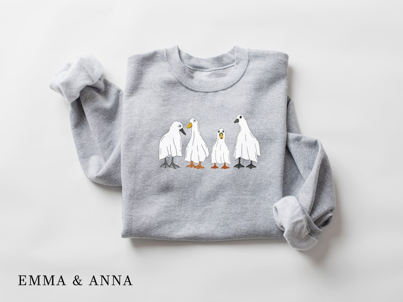 May include: A gray sweatshirt with a graphic of four white ghosts shaped like ducks. The ghosts have orange beaks and black eyes.
