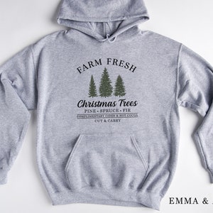 Op de afbeelding: Grijs hooded sweatshirt met de tekst "FARM FRESH" boven een afbeelding van drie naaldbomen en de tekst "Christmas Trees PINE SPRUCE FIR COMPLIMENTARY CIDER & HOT COCOA CUT & CARRY" onder de bomen.