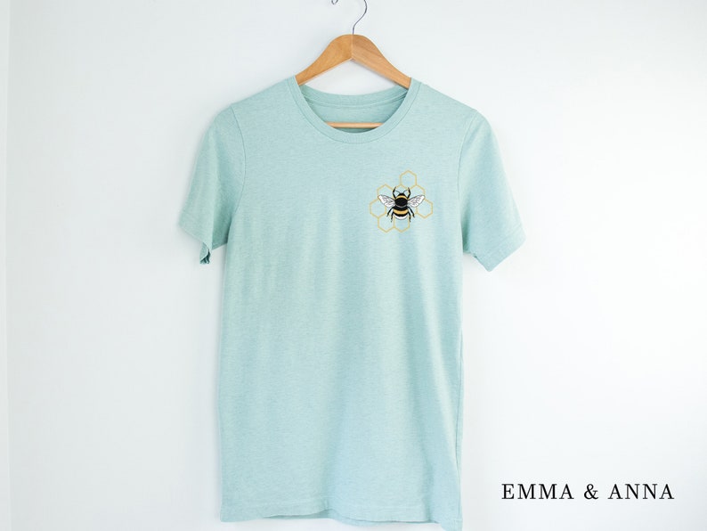 May include: A light blue t-shirt with a bee and honeycomb design embroidered on the front.