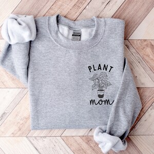 May include: Gray sweatshirt with the text "PLANT MOM" and a simple line drawing of a potted plant.