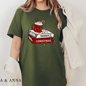 May include: Green t-shirt with a graphic of a mug of hot chocolate with whipped cream and a candy cane on top of a stack of books. The books have the text "Merry Christmas" on them.