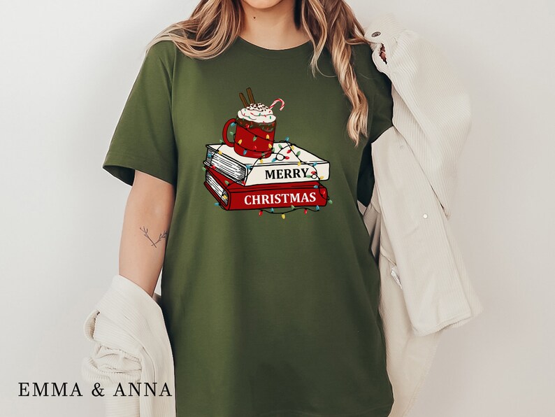 May include: Green t-shirt with a graphic of a mug of hot chocolate with whipped cream and a candy cane on top of a stack of books. The books have the text "Merry Christmas" on them.