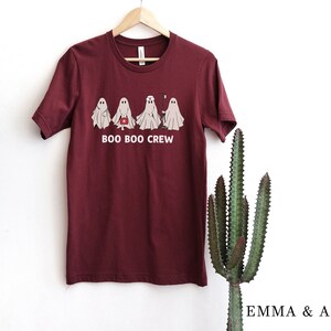 Puede incluir: Camiseta color burdeos con un gr&aacute;fico de cinco fantasmas en l&iacute;nea. Los fantasmas son blancos y tienen ojos negros. El texto "BOO BOO CREW" est&aacute; impreso debajo de los fantasmas.