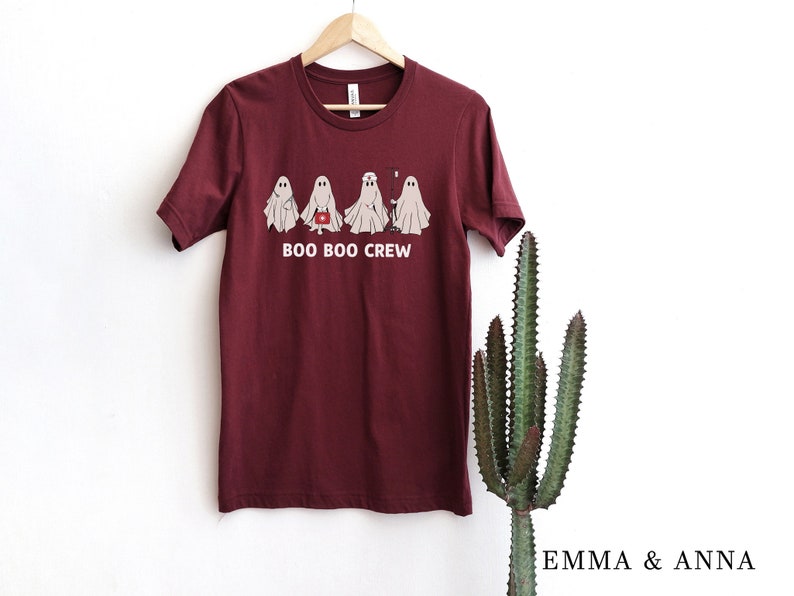 Puede incluir: Camiseta color burdeos con un gr&aacute;fico de cinco fantasmas en l&iacute;nea. Los fantasmas son blancos y tienen ojos negros. El texto "BOO BOO CREW" est&aacute; impreso debajo de los fantasmas.