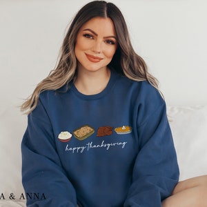 K&ouml;nnte beinhalten: Ein marineblauer Pullover mit einer wei&szlig;en Grafik von Thanksgiving-Lebensmitteln und dem Text "happy thanksgiving".