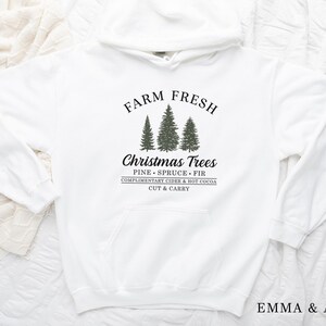 May include: White hoodie with a black graphic that says "Farm Fresh Christmas Trees" with a drawing of three evergreen trees and the text "Pine Spruce Fir Complimentary Cider & Hot Cocoa Cut & Carry".