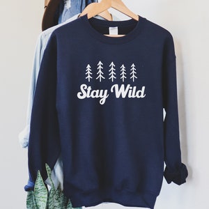 K&ouml;nnte beinhalten: Ein marineblauer Pullover mit einer wei&szlig;en Grafik von Kiefern und dem Text "Stay Wild".