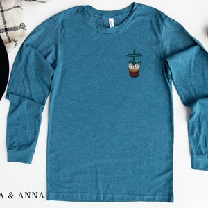 Peut inclure: Un t-shirt &agrave; manches longues bleu sarcelle avec un petit graphique d'un caf&eacute; glac&eacute; sur la poitrine gauche.