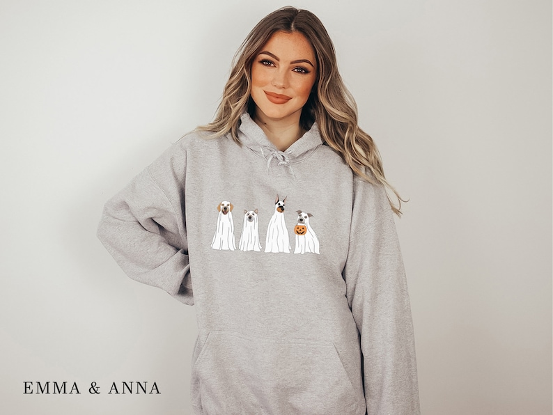 May include: A grey hoodie featuring a graphic of four dogs dressed as ghosts for Halloween. The dogs are wearing white sheets with their heads poking out. The text "EMMA & ANNA" is at the bottom of the image.