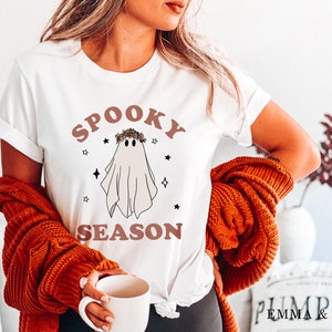 May include: White t-shirt with a ghost wearing a floral crown and the text "Spooky Season" in brown letters.