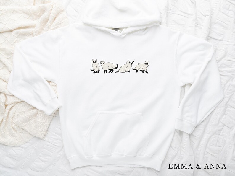 Puede incluir: Sudadera con capucha blanca con un gr&aacute;fico de cuatro gatos blancos con ojos y colas negros. Los gatos est&aacute;n en l&iacute;nea, caminando en la misma direcci&oacute;n.