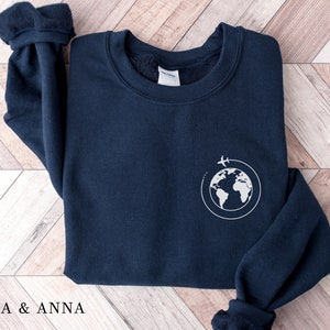 May include: A navy blue sweatshirt with a white graphic of a globe with a plane flying around it.