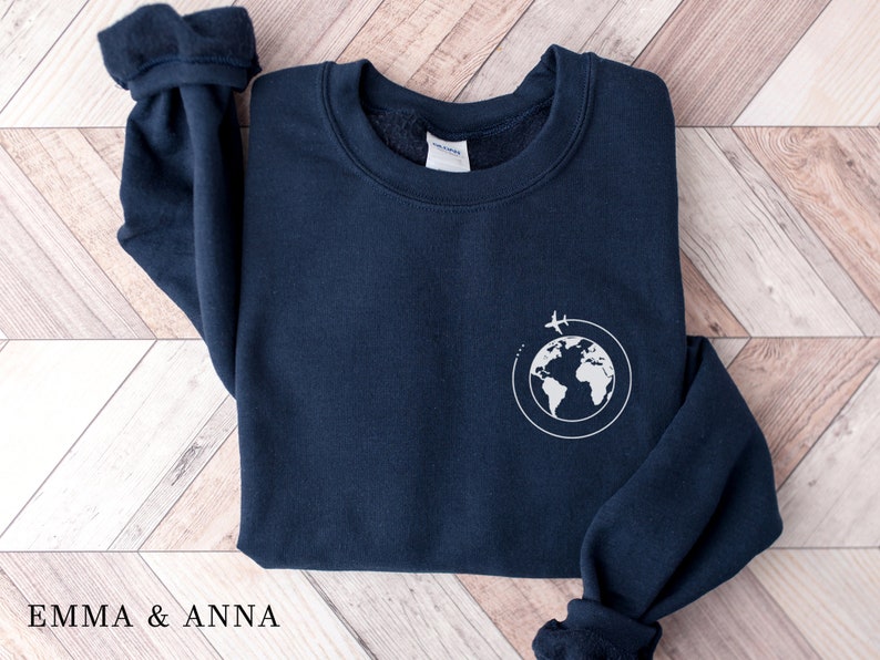 May include: A navy blue sweatshirt with a white graphic of a globe with a plane flying around it.