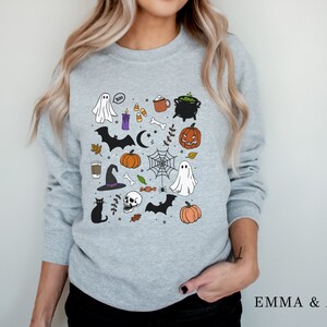 May include: A gray sweatshirt with a Halloween-themed design featuring ghosts, bats, pumpkins, a cauldron, a witch's hat, a skull, candy corn, and other spooky elements.