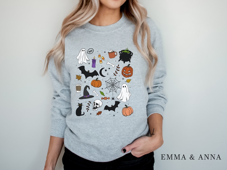 May include: A gray sweatshirt with a Halloween-themed design featuring ghosts, bats, pumpkins, a cauldron, a witch's hat, a skull, candy corn, and other spooky elements.
