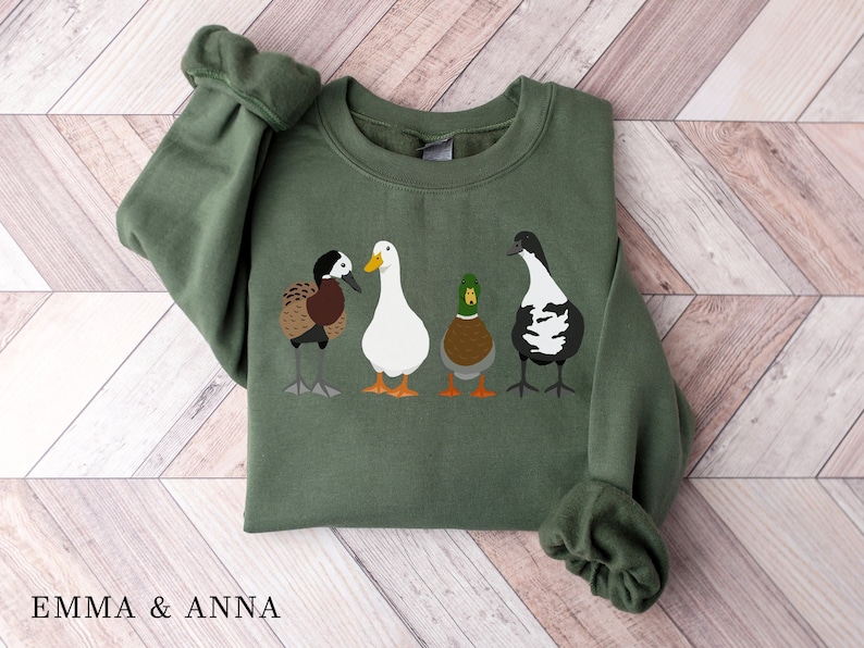 Peut inclure: Un sweat-shirt vert avec un motif de quatre canards align&eacute;s. Les canards sont de couleurs diff&eacute;rentes et ont des marques diff&eacute;rentes. Le sweat-shirt a un col rond et des manches longues.