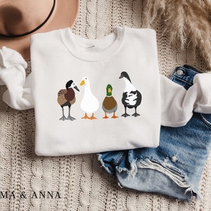 Peut inclure: Sweat-shirt blanc avec un motif de quatre canards align&eacute;s. Les canards sont brun, blanc, vert et noir et blanc.