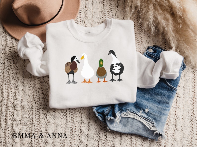 Peut inclure: Sweat-shirt blanc avec un motif de quatre canards align&eacute;s. Les canards sont brun, blanc, vert et noir et blanc.