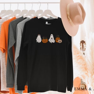 May include: Black long-sleeve shirt with a graphic of ghosts and pumpkins. The shirt is hanging on a rack with other shirts.