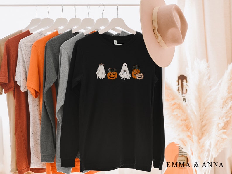 May include: Black long-sleeve shirt with a graphic of ghosts and pumpkins. The shirt is hanging on a rack with other shirts.