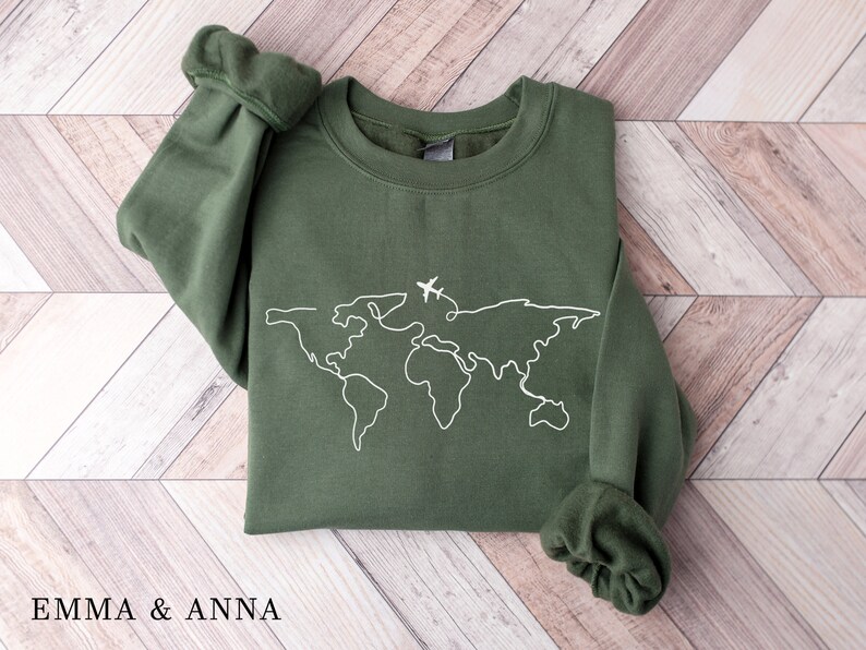 May include: A green sweatshirt with a white outline of the world and a small airplane above it. The text "EMMA & ANNA" is at the bottom of the image.