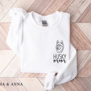 Pode incluir: Camisola branca com um desenho de linha preta de um c&atilde;o husky e o texto "HUSKY MOM" na frente.