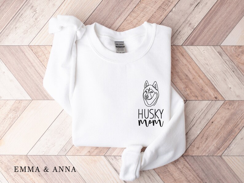 Pode incluir: Camisola branca com um desenho de linha preta de um c&atilde;o husky e o texto "HUSKY MOM" na frente.