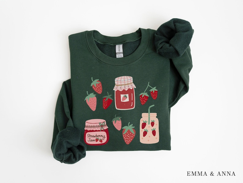 May include: A dark green sweatshirt with a graphic design of jars of strawberry jam and strawberries. The text on one of the jars reads "Strawberry Jam".