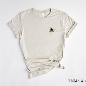 May include: A beige t-shirt with a bee and honeycomb design on the left chest.