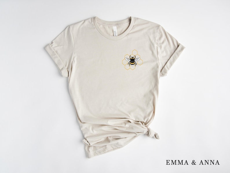 May include: A beige t-shirt with a bee and honeycomb design on the left chest.