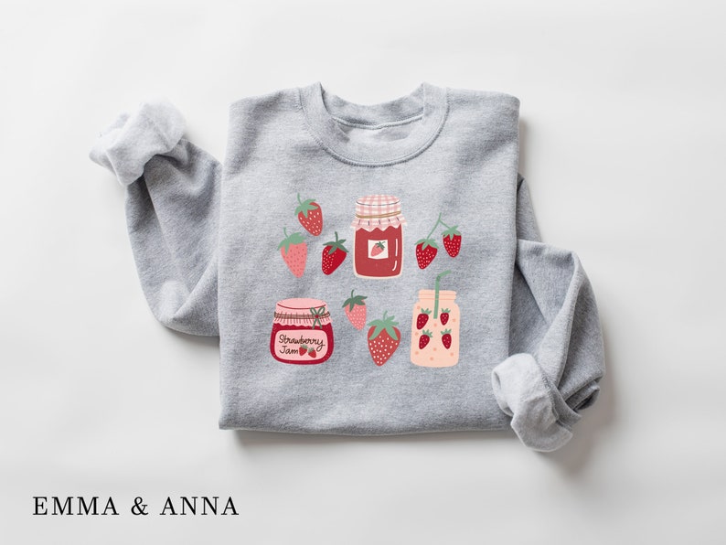 May include: Gray sweatshirt with a strawberry jam jar, a glass of strawberry juice, and strawberries printed on it. The text "Strawberry Jam" is printed on the jar.