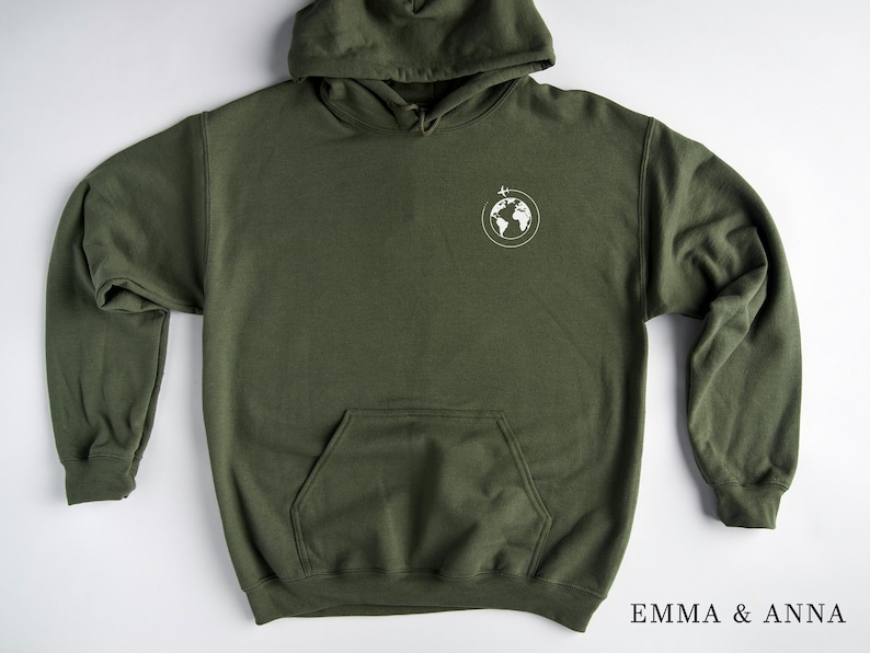 May include: A dark green hooded sweatshirt with a white graphic of a globe with a plane flying over it. The text "EMMA & ANNA" is printed on the bottom right corner of the image.