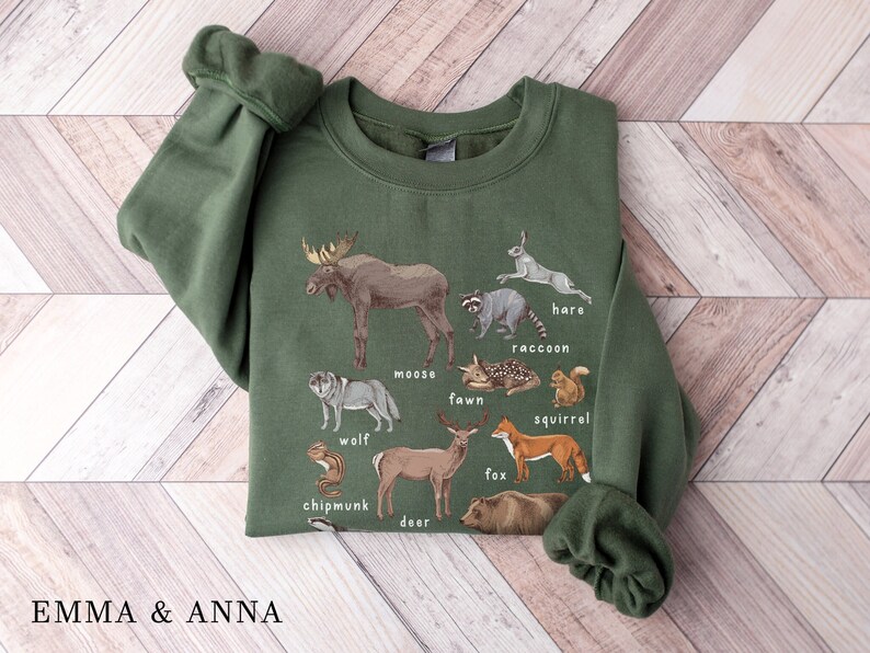 May include: A green sweatshirt with a graphic print of various forest animals, including a moose, wolf, deer, fox, squirrel, chipmunk, raccoon, hare, and fawn. The animals are labeled with their names.