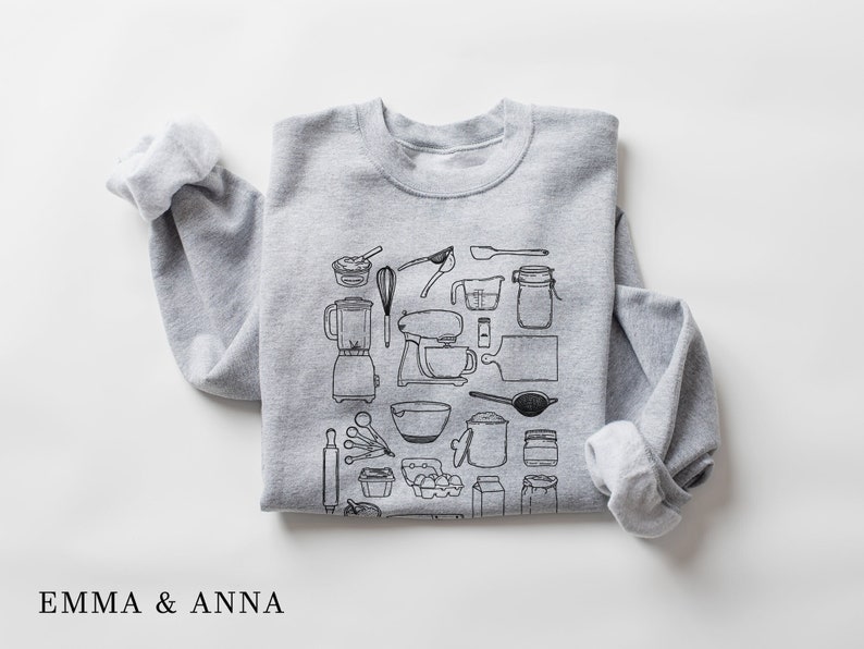 May include: Gray sweatshirt with a black and white illustration of kitchen tools and appliances. The illustration includes a blender, mixer, rolling pin, measuring cups, and more.