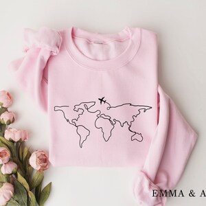 May include: A pink sweatshirt with a black outline of the world and two airplanes on it. The text "EMMA & ANNA" is printed on the bottom of the sweatshirt.