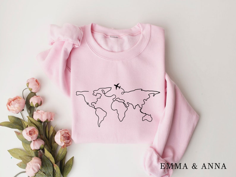 May include: A pink sweatshirt with a black outline of the world and two airplanes on it. The text "EMMA & ANNA" is printed on the bottom of the sweatshirt.