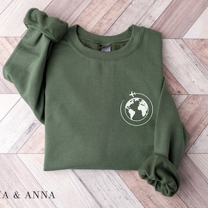 May include: A green sweatshirt with a white graphic of a globe with airplanes flying around it.