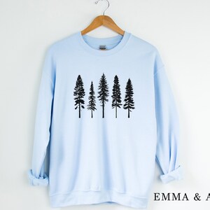 May include: A light blue sweatshirt with a black silhouette of five pine trees on the front. The sweatshirt has long sleeves and a crew neck.