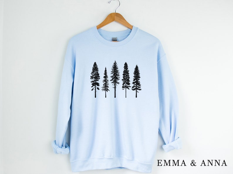 May include: A light blue sweatshirt with a black silhouette of five pine trees on the front. The sweatshirt has long sleeves and a crew neck.