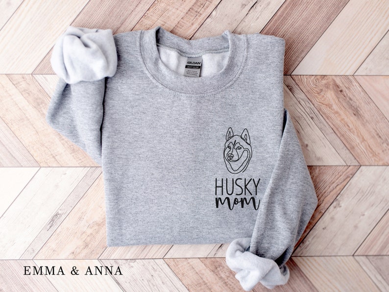 Pode incluir: Camisola cinzenta com um contorno preto de um c&atilde;o husky e o texto "Husky Mom" na frente.