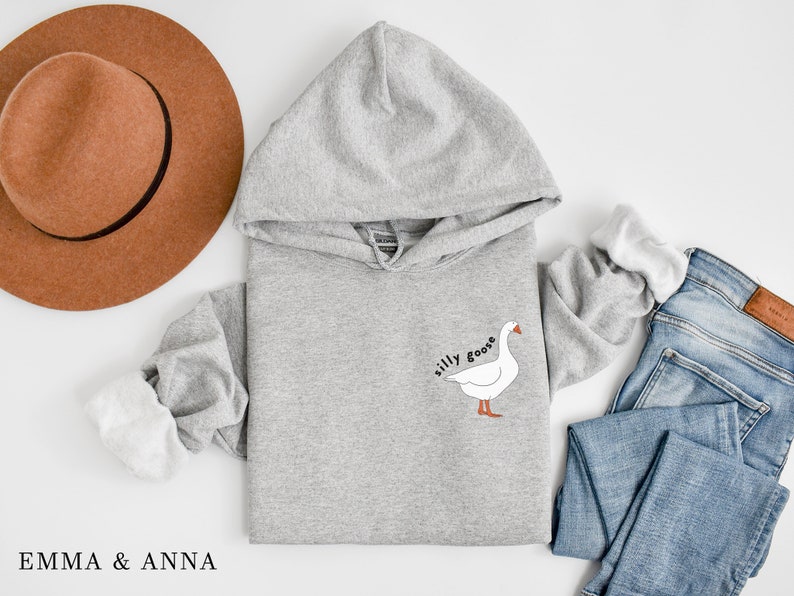 K&ouml;nnte beinhalten: Ein grauer Kapuzenpullover mit einer wei&szlig;en G&auml;nse-Illustration und dem Text "silly goose" auf der Vorderseite.