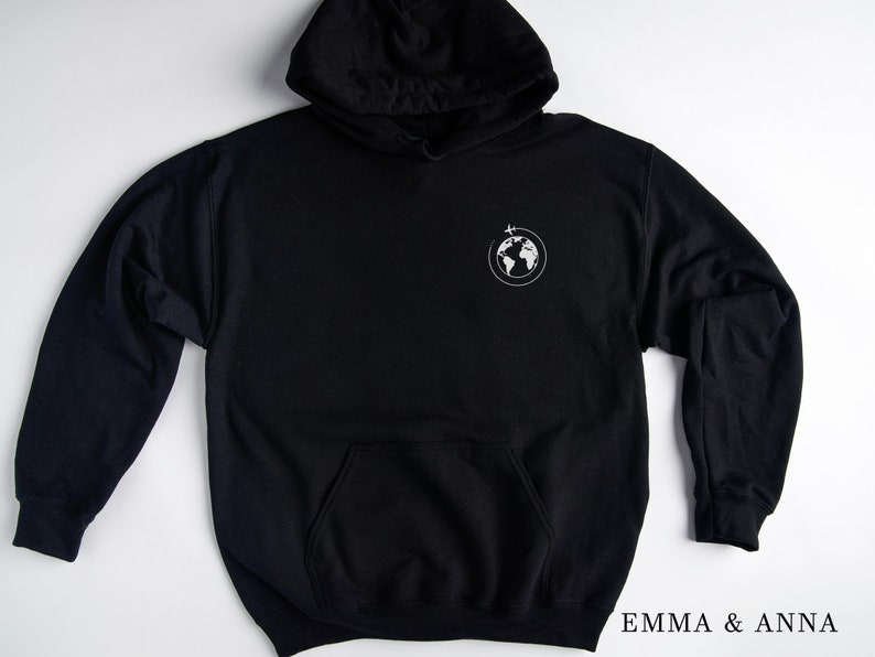 May include: Black hooded sweatshirt with a white graphic of a globe with a plane flying above it. The text "EMMA & ANNA" is printed on the bottom right corner of the image.
